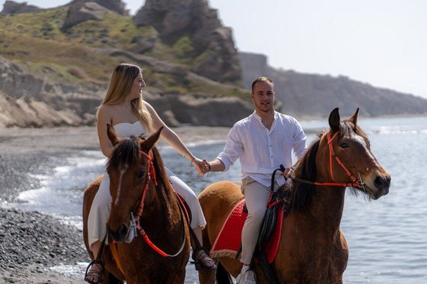 Two people riding horses on a beach with rocky cliffs in the background. 5