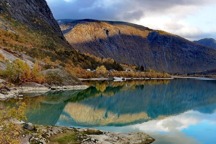 A calm lake with clear reflections, surrounded by mountains and autumn-colored trees. 2