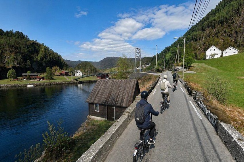 Un camino estrecho con ciclistas, un río y un pequeño edificio de madera. 2