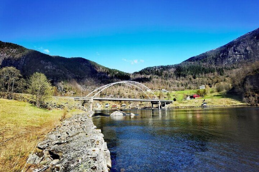 A stone bridge over a river, surrounded by mountains and a clear blue sky. 5