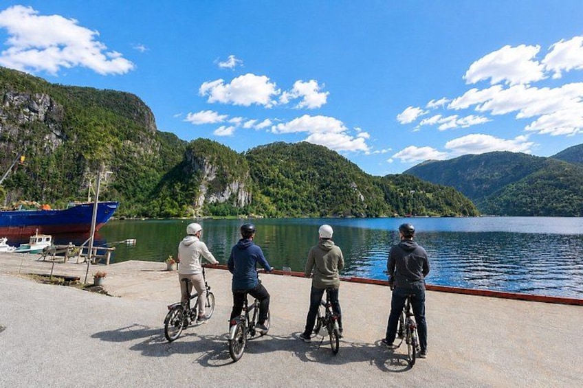 Vier personen op fietsen aan een meer, met bergen op de achtergrond. 1