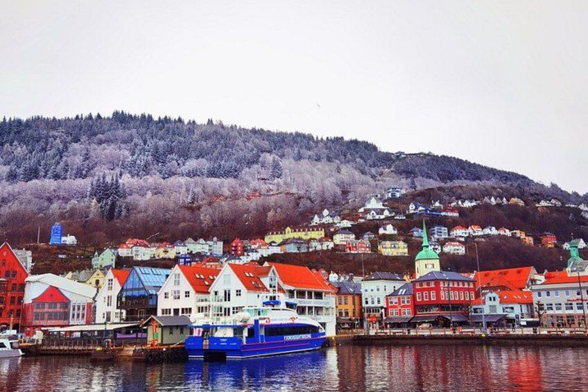 A coastal town with colorful buildings, a blue boat, and a hill with trees in the background. 2