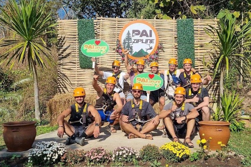 A group of people in helmets and harnesses posing in front of a sign that reads 'PAI ZIPLINE.' 3