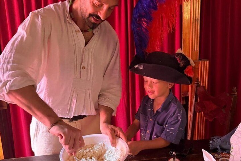 Una persona con camisa blanca mezclando ingredientes en un tazón, con un niño de camisa azul y sombrero negro al fondo. 2
