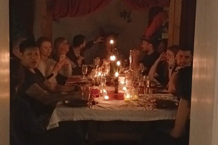 Un grupo de personas sentadas en una mesa con velas y copas, indicando una reunión social o una cena. 1