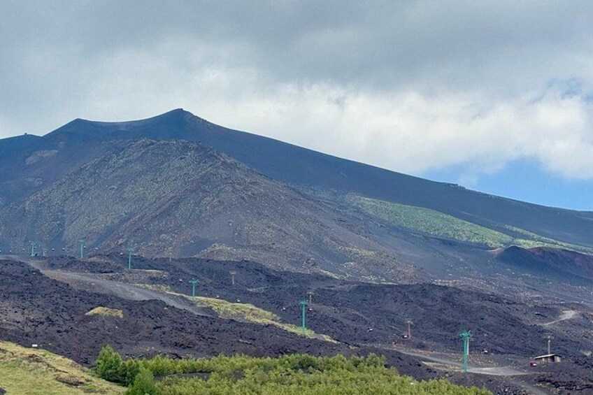 Ett vulkaniskt landskap med ett framträdande berg, spridda gröna växter och en klar himmel. 5