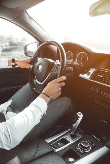 A person driving a car, holding the steering wheel, with a gear shift and dashboard visible. 2