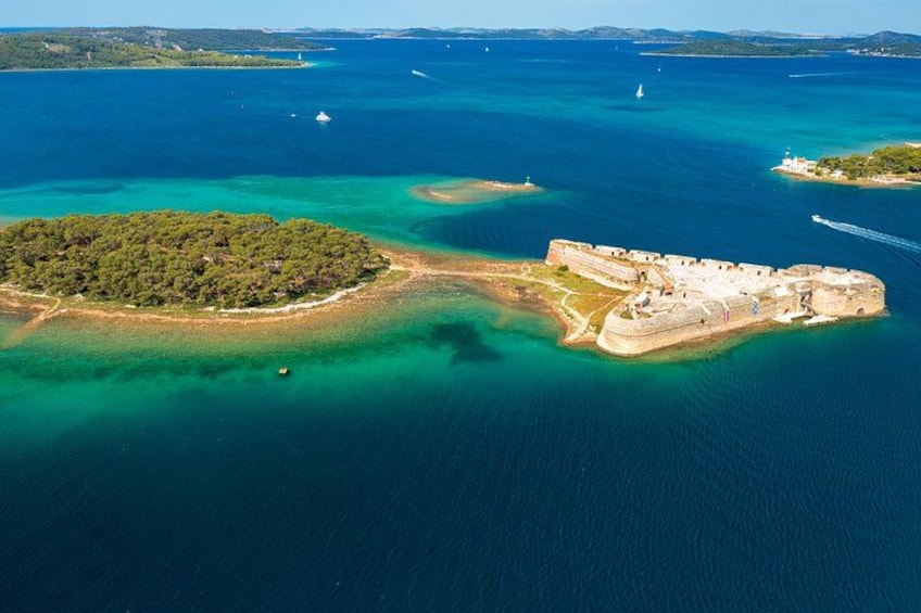 An aerial view of a coastal fortification surrounded by clear blue waters and a small island with dense greenery. 3