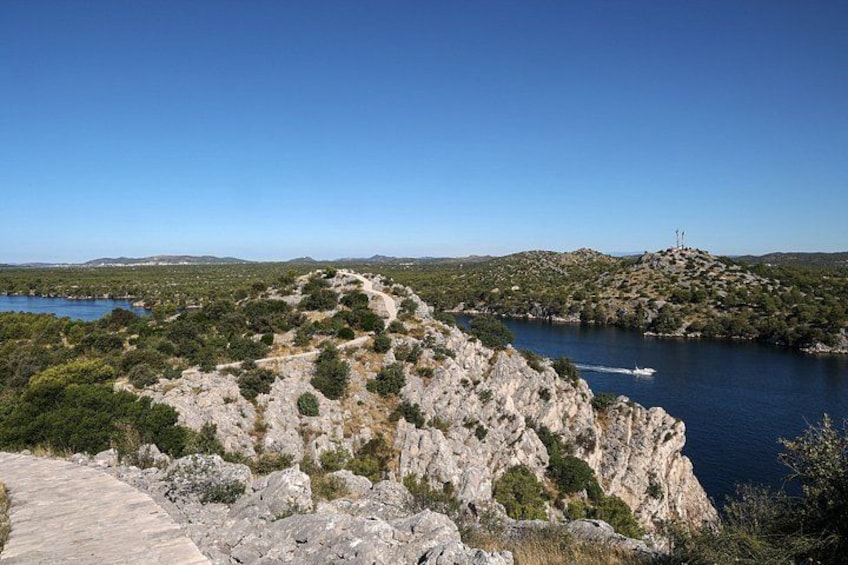 A rocky coastline with a clear blue sky, a body of water, and a distant hill with a structure on top. 4
