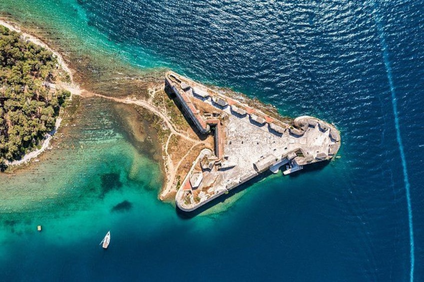 An aerial view of a coastal fortification with a surrounding lagoon and a small boat in the water. 1