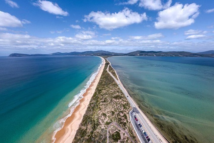 A coastal road curving along a beach with clear blue waters and distant hills. 4