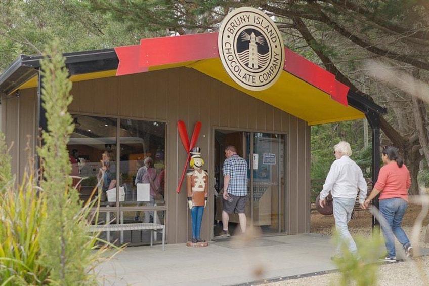 Een gebouw met een bord voor Bruny Island Chocolate Company, een houten constructie met een rood en geel dak, en een persoon die voorbijloopt. 4