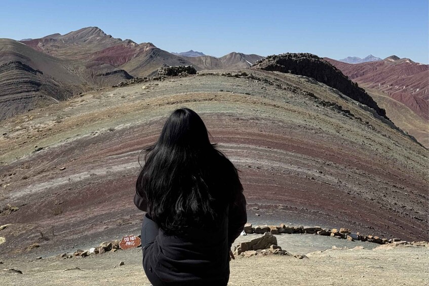 A person standing on a rocky outcrop overlooking a mountainous landscape with layered rock formations. 1