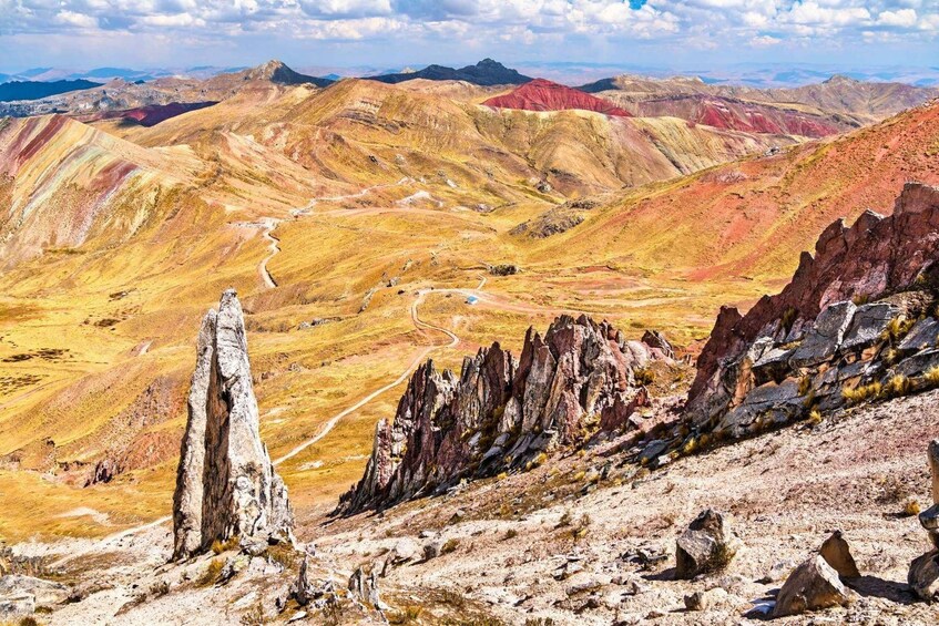 A rugged mountain landscape with a winding road, a prominent rock formation, and distant peaks. 2