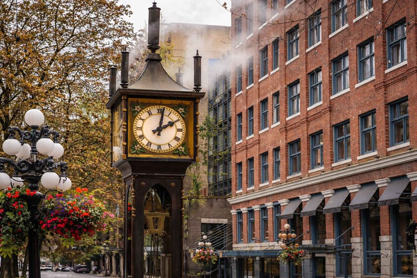 A historic clock tower with Roman numerals, surrounded by brick buildings and autumn foliage. 1