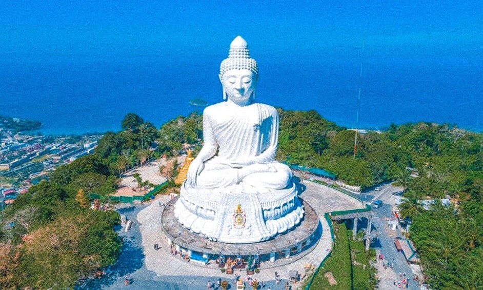 A large white Buddha statue surrounded by a circular walkway, with a coastal background. 2