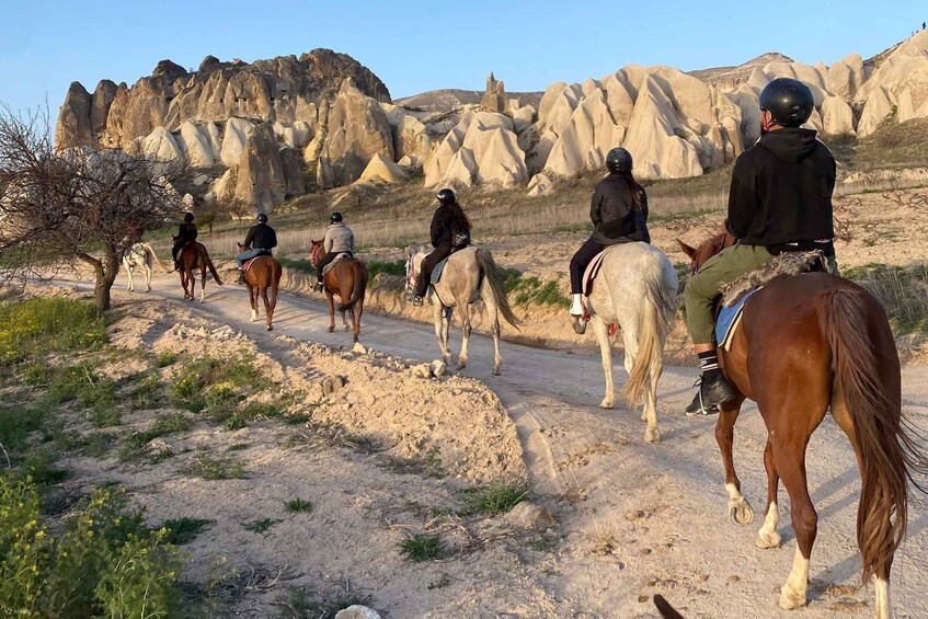 A group of people horseback riding on a dirt path with a rocky mountainous landscape in the background. 2
