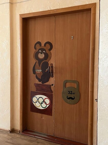 A wooden door with a bear cutout, Olympic rings, and a kettlebell symbol. 3