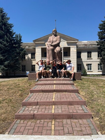 A statue of a seated figure with a group of people sitting on steps in front of a building. 2