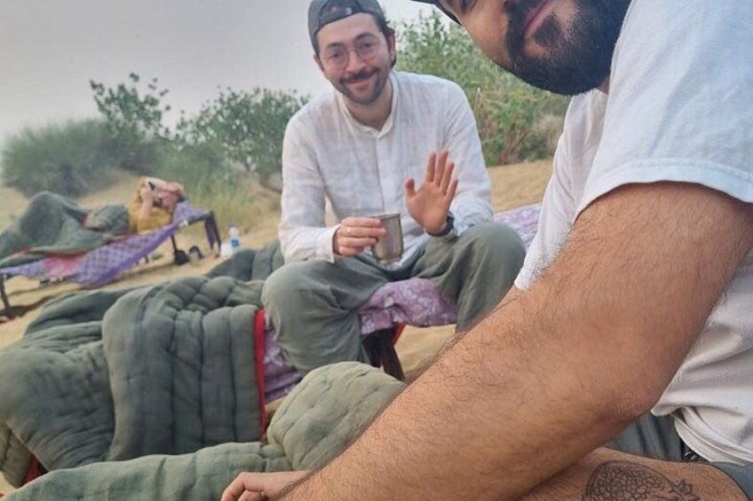 Two people sitting on a blanket outdoors, one holding a cup. 3