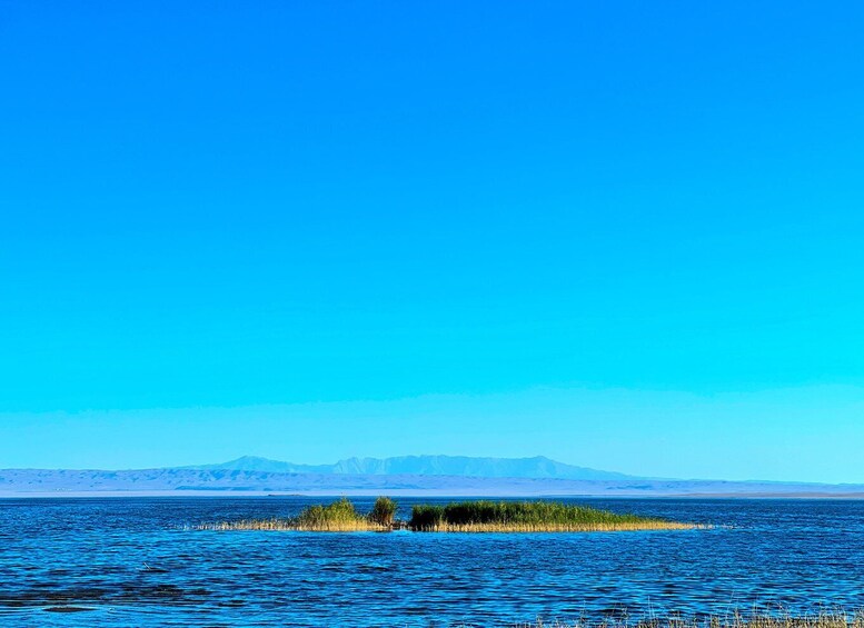 Un lago tranquilo con una pequeña isla en el centro, rodeado de montañas a lo lejos. 3