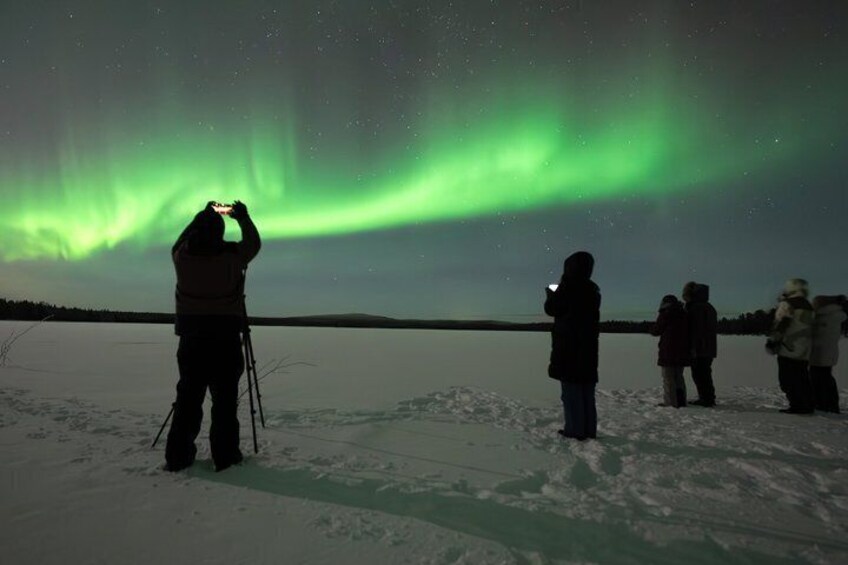 Folk betragter nordlys over et snelandskab. 2