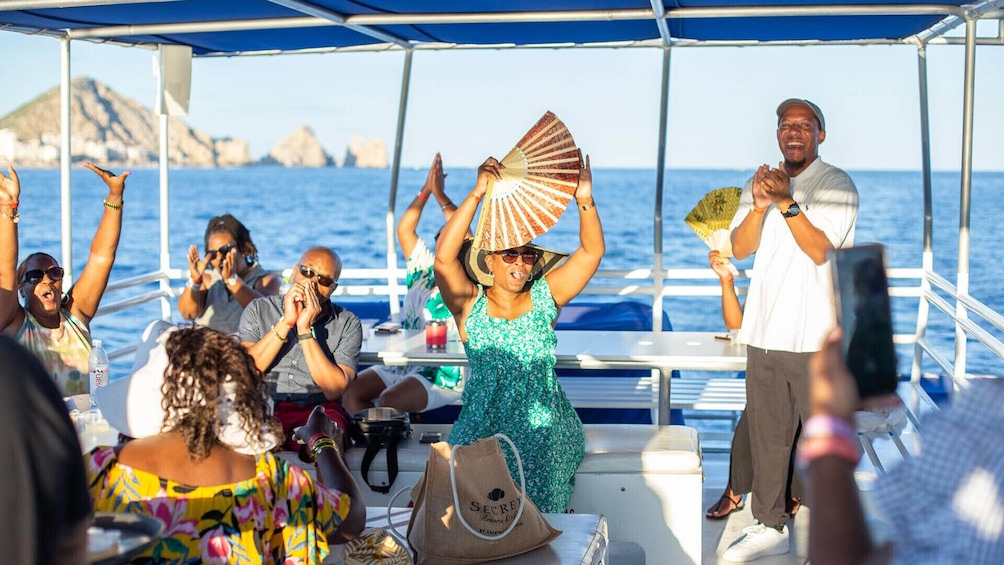 A group of people on a boat with a woman holding a fan, and rocky cliffs in the background. 1