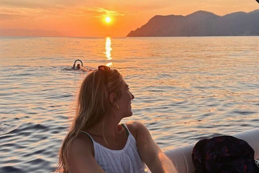 Iemand zit aan een waterlichaam tijdens de zonsondergang, met bergen op de achtergrond. 1
