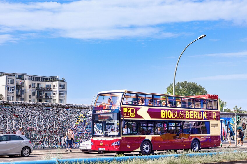 Un autobús de dos pisos con la leyenda 'BIGBUS BERLIN' en su lateral, estacionado en una calle con un mural al fondo. 1