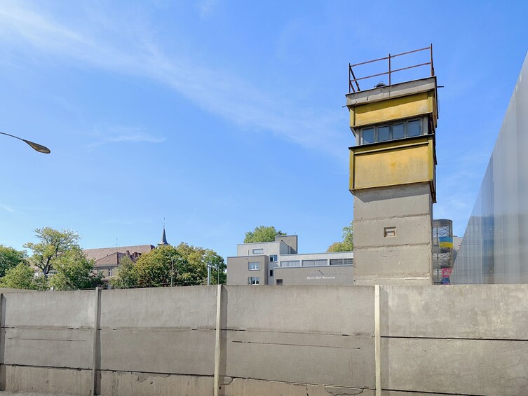Una barrera de hormigón, una torre amarilla y gris, y el Memorial del Muro de Berlín al fondo. 4