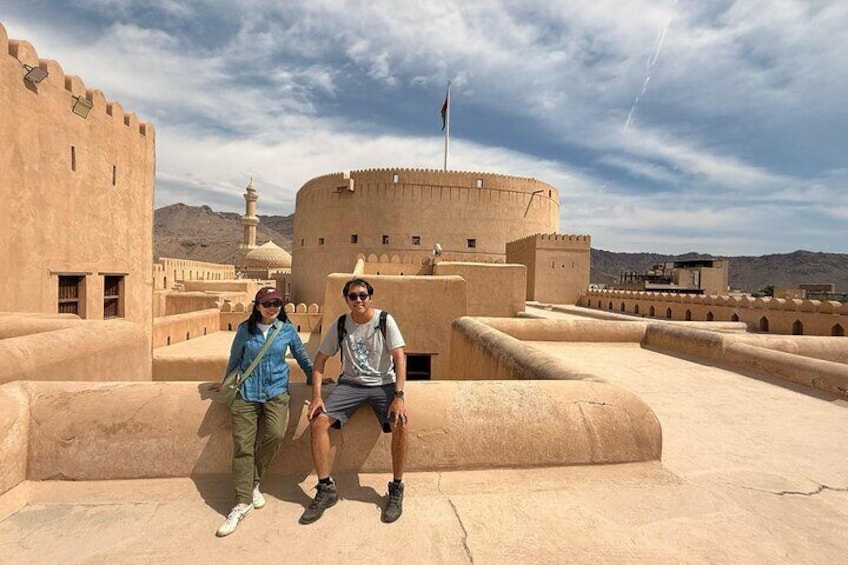 Two people sitting on a terrace with a large fortress-like structure in the background. 1