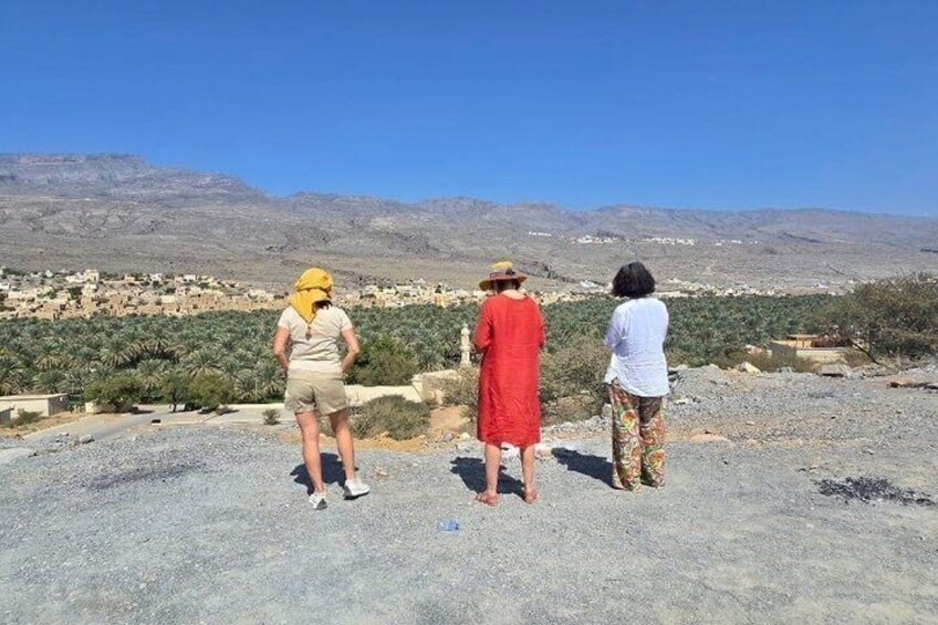 Three people standing on a gravel surface, overlooking a town and mountains in the distance. 5