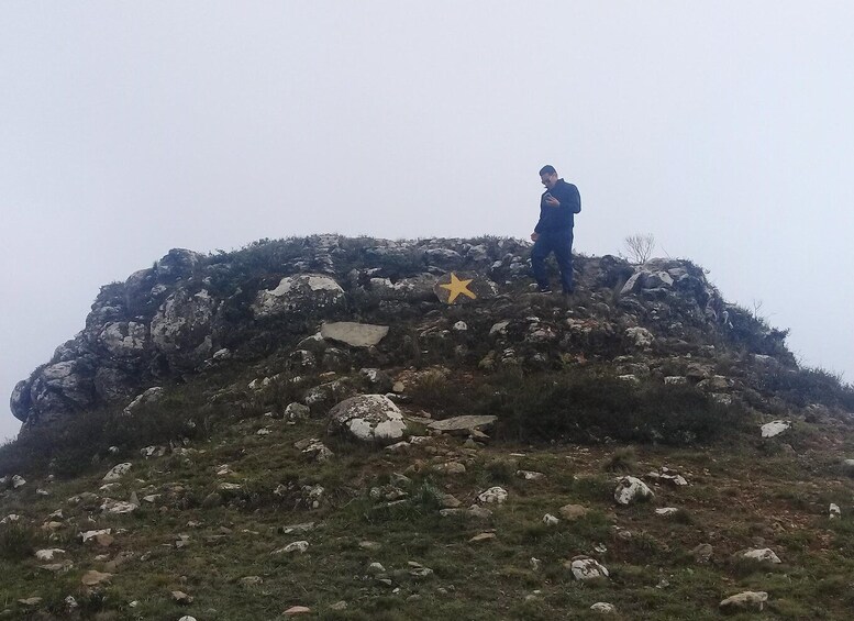 A person standing on a rocky hill with sparse vegetation. 4