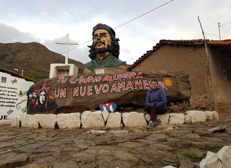A large mural with a figure and text, a cross, and a person sitting on a stone wall. 5