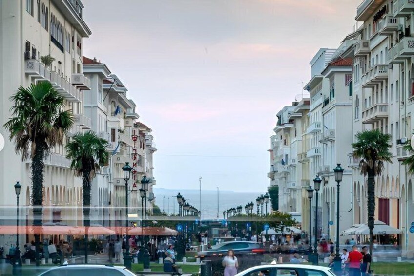 A coastal promenade with palm trees, a blue tram, and people walking. 5
