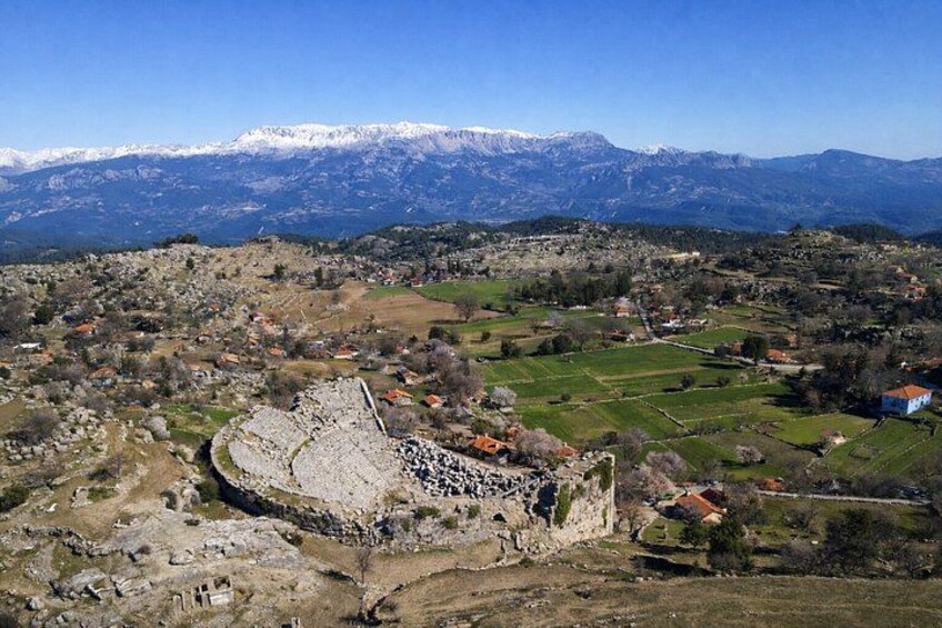 Un paisaje montañoso con una estructura de piedra histórica, casas dispersas y campos. 2