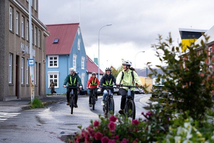 Three cyclists on a wet road with buildings and a blue house in the background. 2