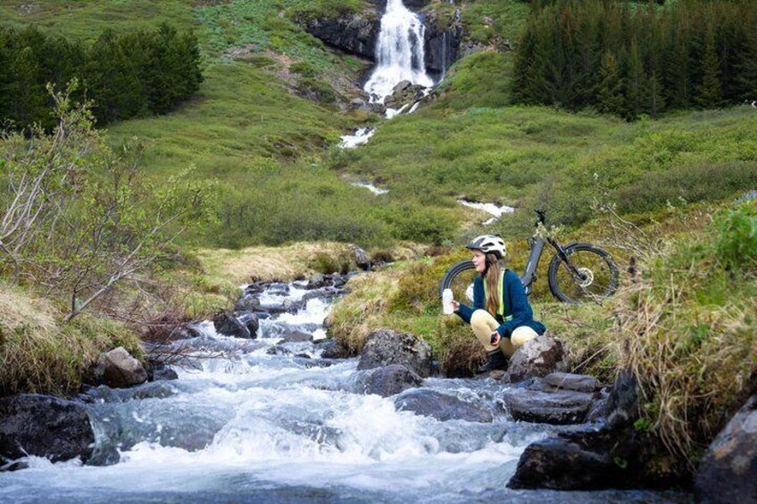 A person sitting by a flowing river with a bicycle and a water bottle. 3