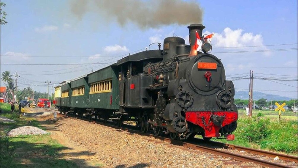 A steam locomotive with a red front, emitting steam, on a railway track. 5