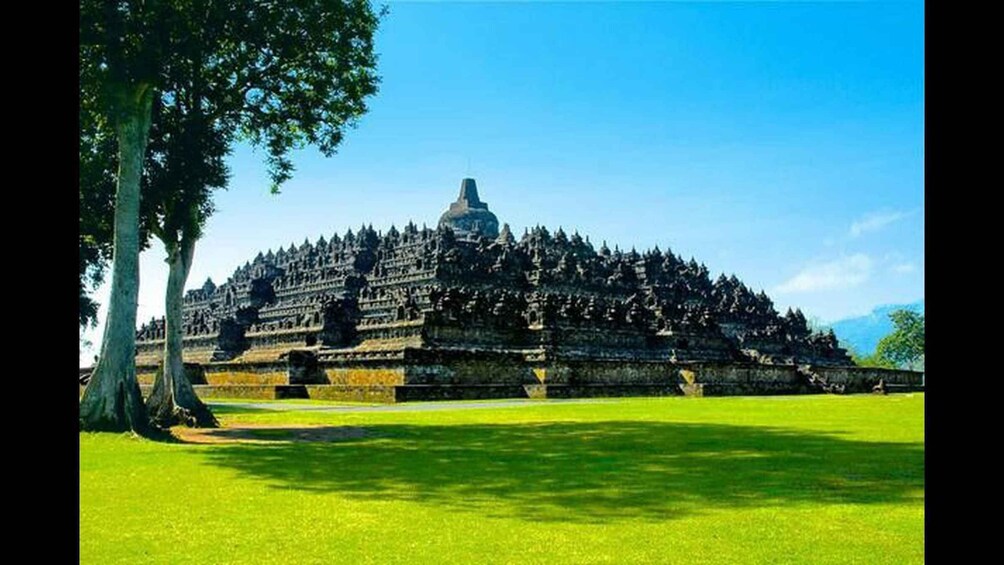 A large, tiered temple complex with a central dome, surrounded by lush green grass and trees. 1
