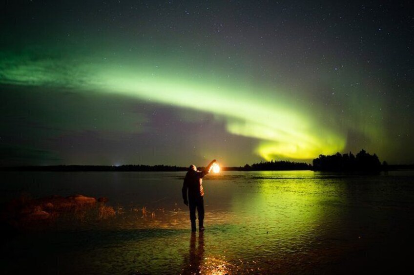 En person står ved vandet om natten og ser nordlys. 1