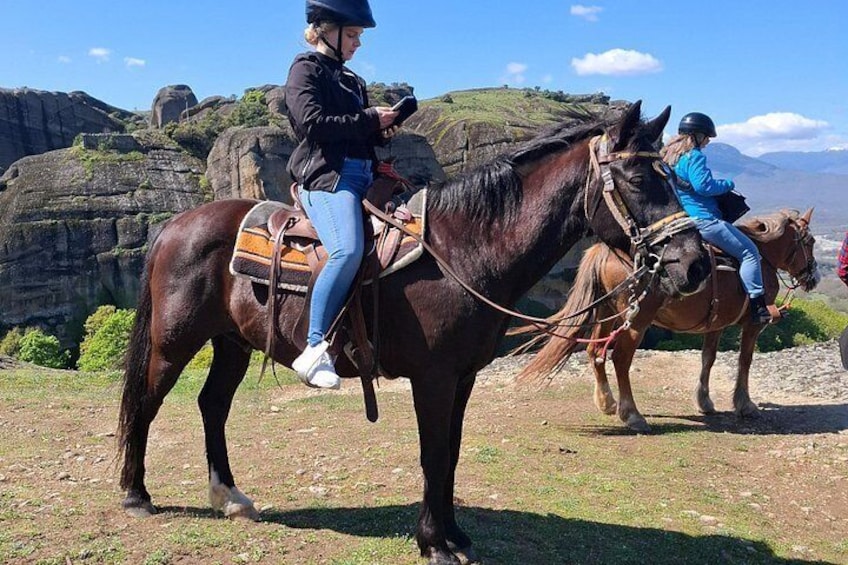 Two people riding horses on a rocky terrain with a mountainous backdrop. 4