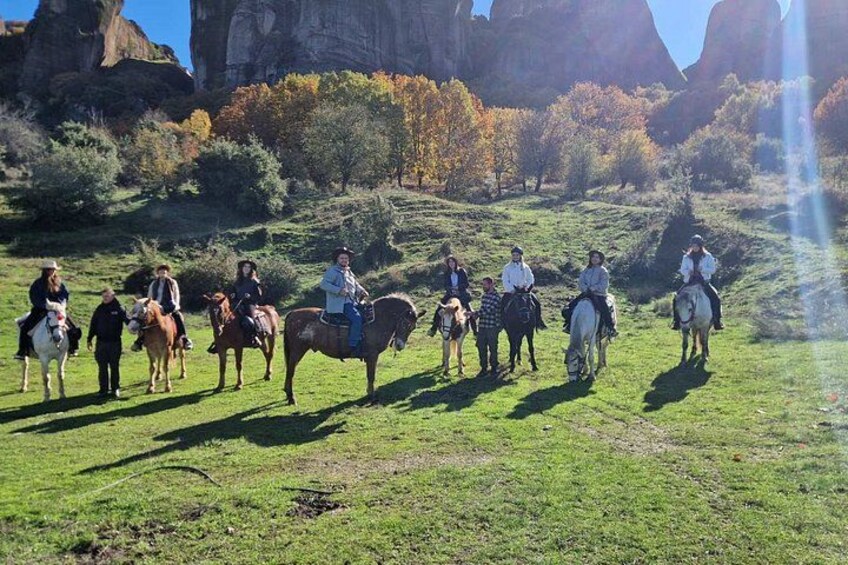 A group of people horseback riding on a grassy field with rocky formations in the background. 2