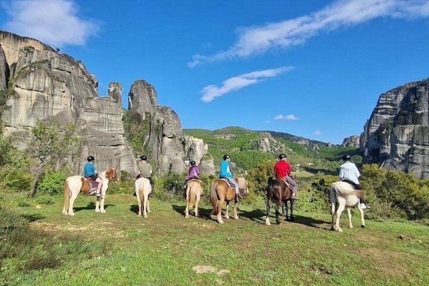 A group of people on horseback in a grassy area with rock formations in the background. 5