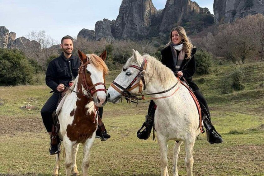 Two people riding horses in a grassy field with rocky mountains in the background. 5