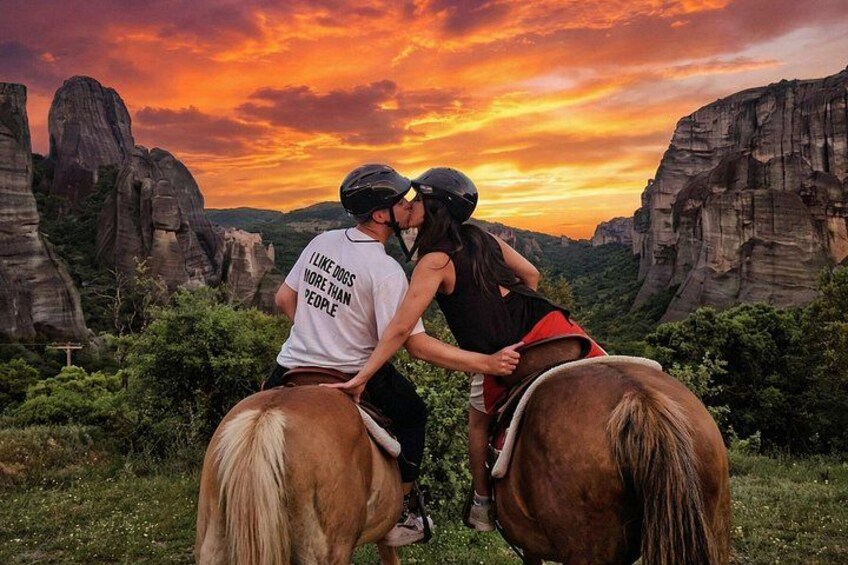 Two people on horseback in a natural landscape with rock formations and a sunset. 1