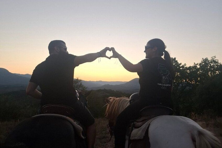 Two people on horseback making a heart shape with their hands against a sunset backdrop. 4