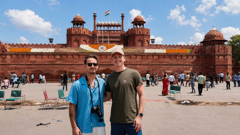 Two people standing in front of a large red building with domes and a flag. 5