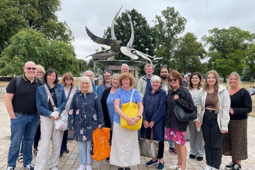 Eine Gruppe von Menschen steht in einem Park, im Hintergrund steht eine Vogelstatue. 3