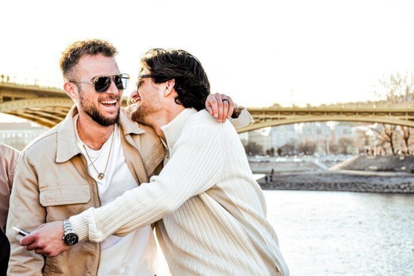 Two people embracing near a river with a bridge in the background. 5